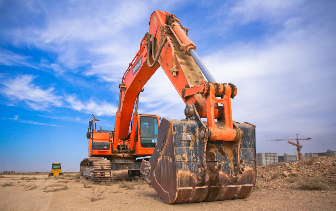 hero-img-02 A large orange excavator working on a construction site under a blue sky.