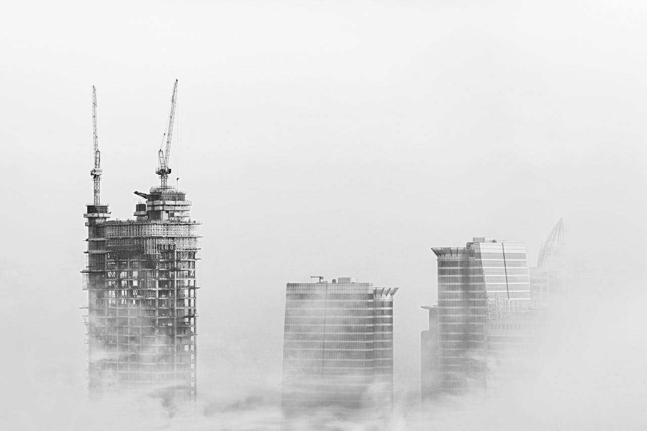 gallery-3 Black and white photo of Dubai skyline with skyscrapers and cranes emerging from fog, showcasing urban development.