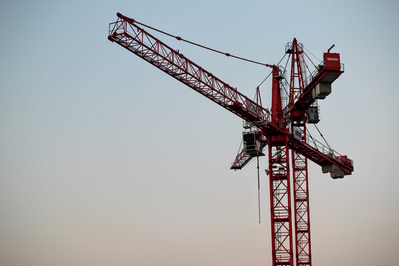 services-02 A red tower crane on a construction site set against a clear sky during daytime.