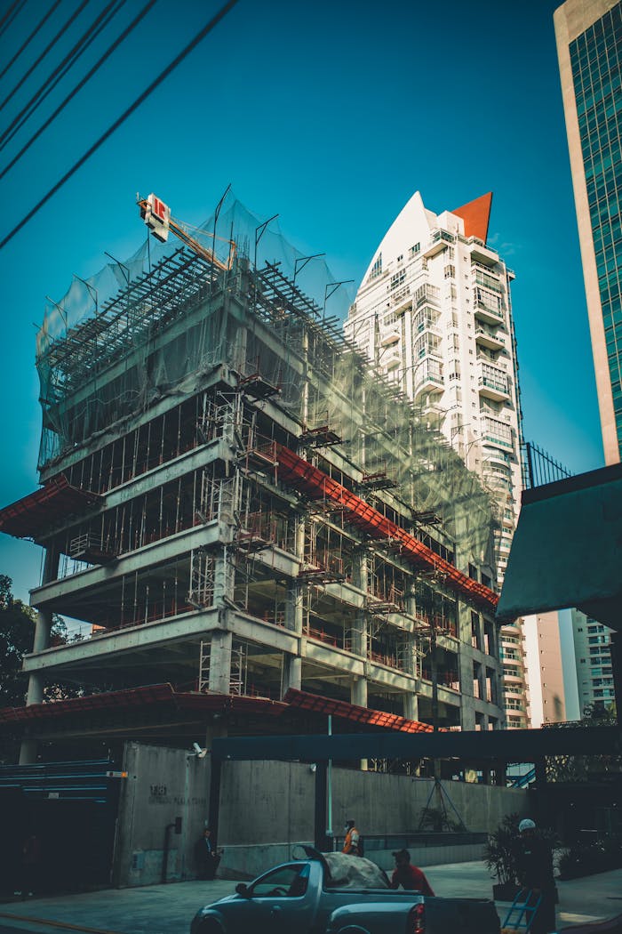 gallery-2 High-rise building under construction with scaffolding and crane in urban cityscape.