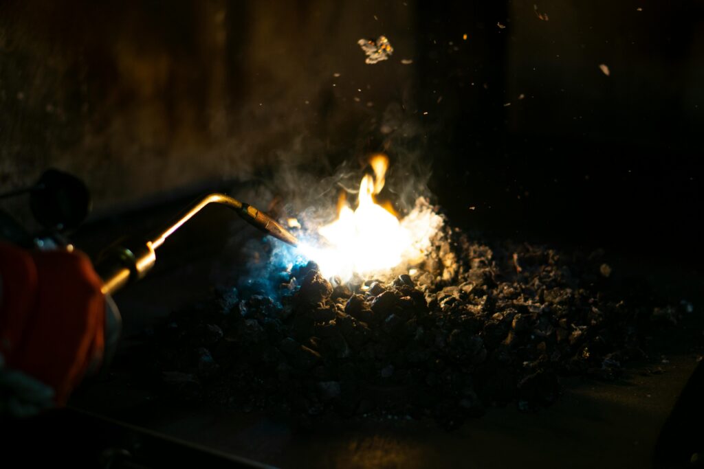pexels photo 3997249 3997249 Close-up of a torch flame heating charcoal, emitting smoke in an industrial setting.