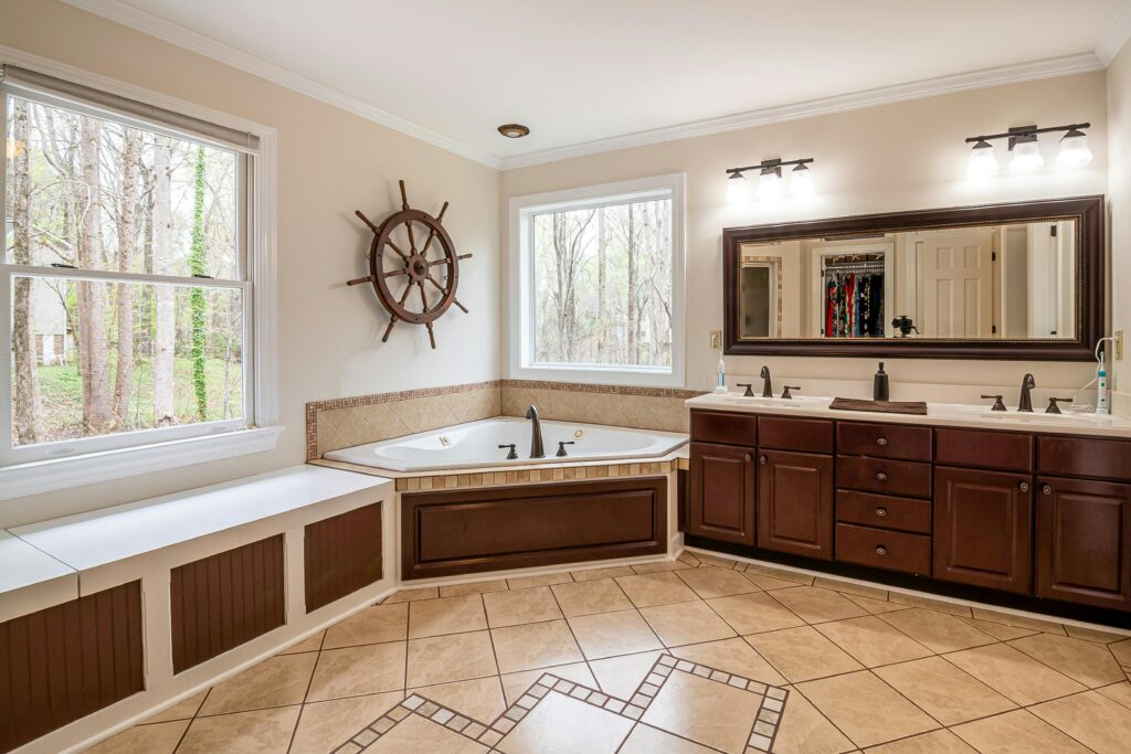 pexels photo 4030050 4030050 Spacious bathroom featuring a large corner bathtub, wooden cabinets, and natural light from large windows.
