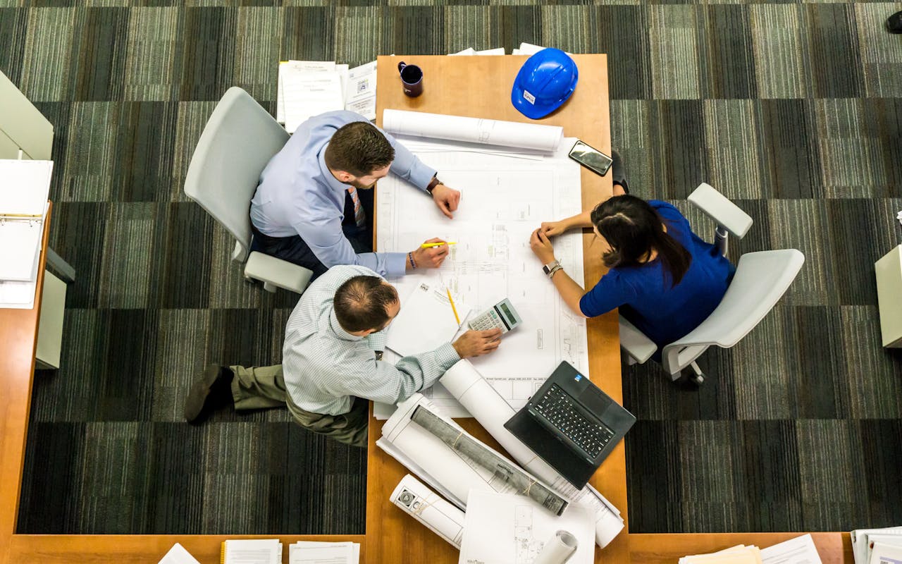 our-services-1 Top view of a team working on construction plans in an office setting.